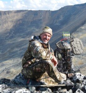 Chuck Trover wears camo and sits with archery gear.