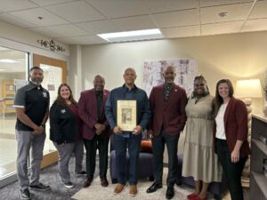 SIU Chancellor Austin Lane and members of the admissions team meet with Dennis Goins, director of BDTV at Ben Davis High School and former Saluki basketball player, who holds a framed photo from his playing days at SIU.