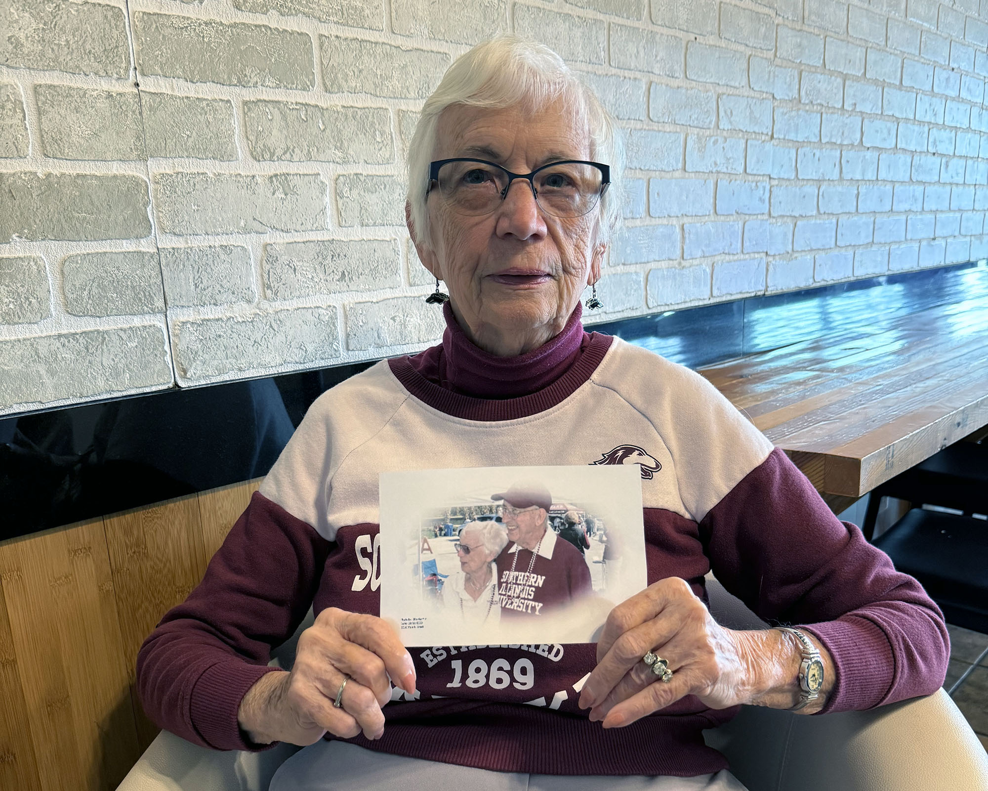 Amber Hanson wears Saluki gear and holds a photo of her and her late husband, Homer Hanson, at a Saluki event.