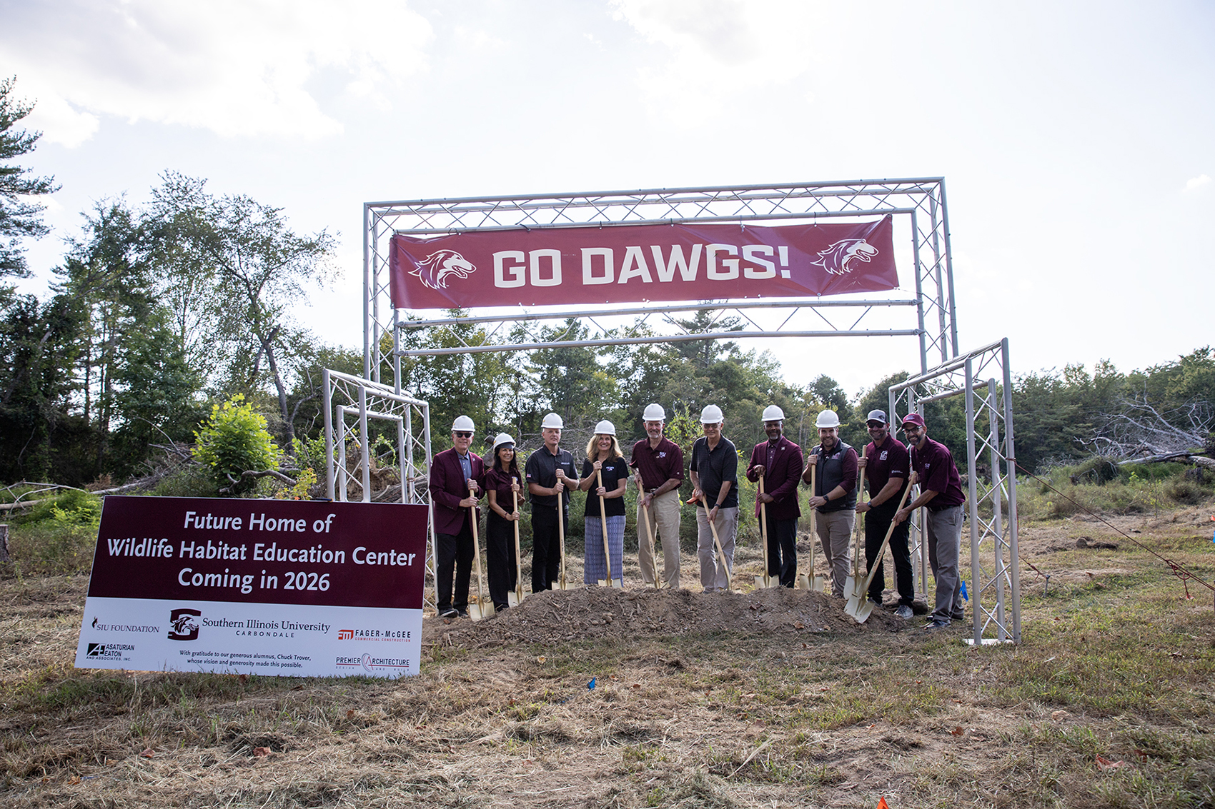 A group of SIU leaders, donor Chuck Trover, his family, and project partners stand with shovels during the groundbreaking for the Wildlife Habitat Education Center at Touch of Nature Outdoor Education Center. A banner reading “Go Dawgs!” hangs overhead.