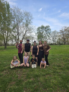 Rebecca VanLuvender and her eight siblings stand for a photo in a grassy field with trees in the background.