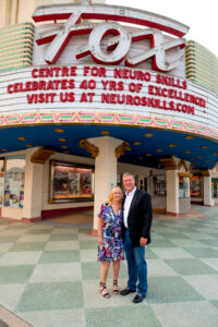 Dr. Mark Ashley and Susan Ashley stand together outside the historic Fox Theater beneath a marquee reading “Centre for Neuro Skills Celebrates 40 Yrs of Excellence,” marking the organization’s milestone anniversary.