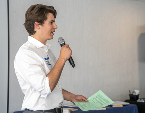 Phillip Hartke speaks into a microphone while holding notes during a campus event.