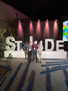Phillip Hartke, center, stands with two peers in front of large “St. Jude” letters at a conference event.