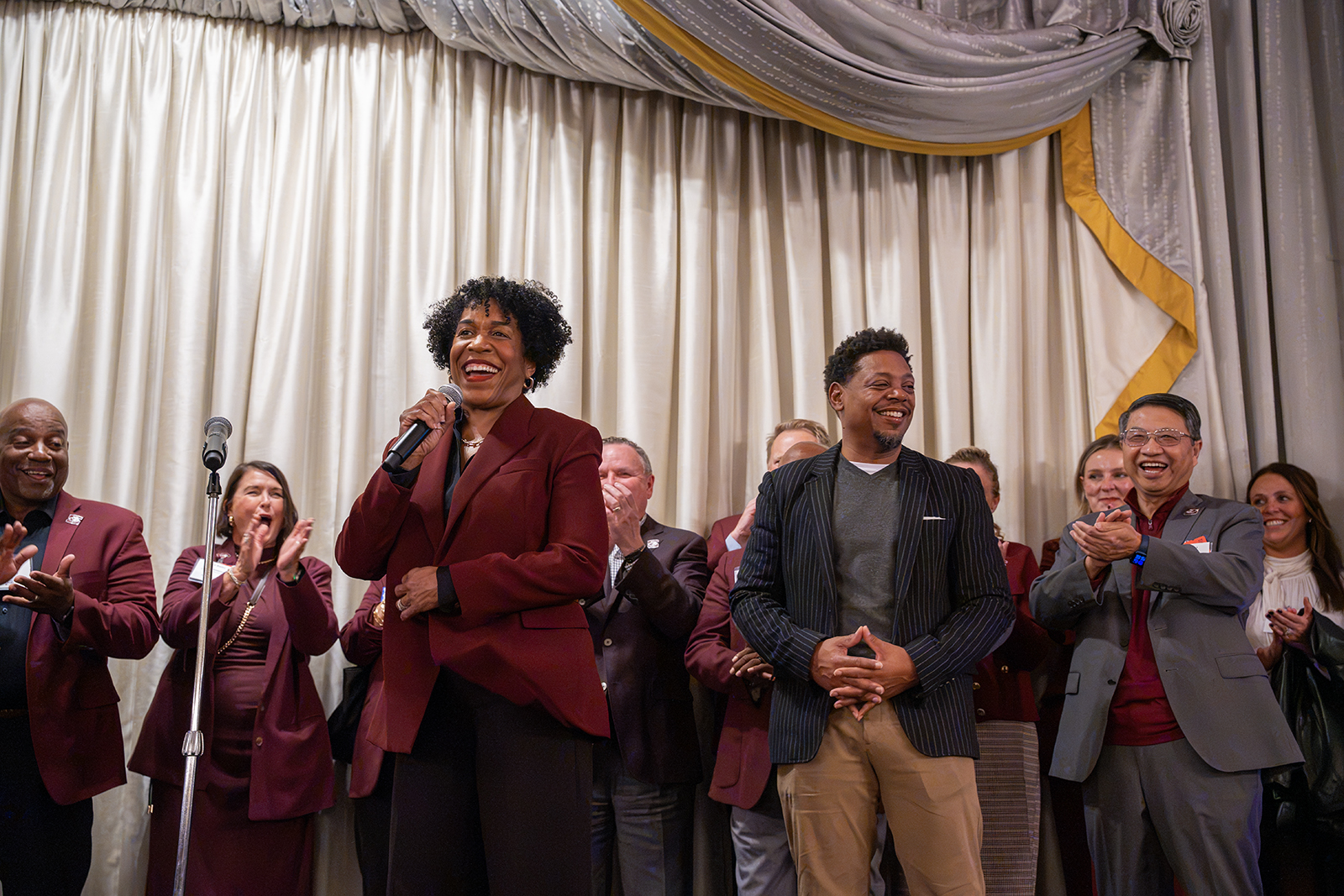 Illinois Lt. Gov. Juliana Stratton smiles while speaking into a microphone alongside her husband, SIU alumnus Bryan Echols, as university leaders and supporters applaud during the Saluki Takeover Tour Chancellor's Reception in Chicago.