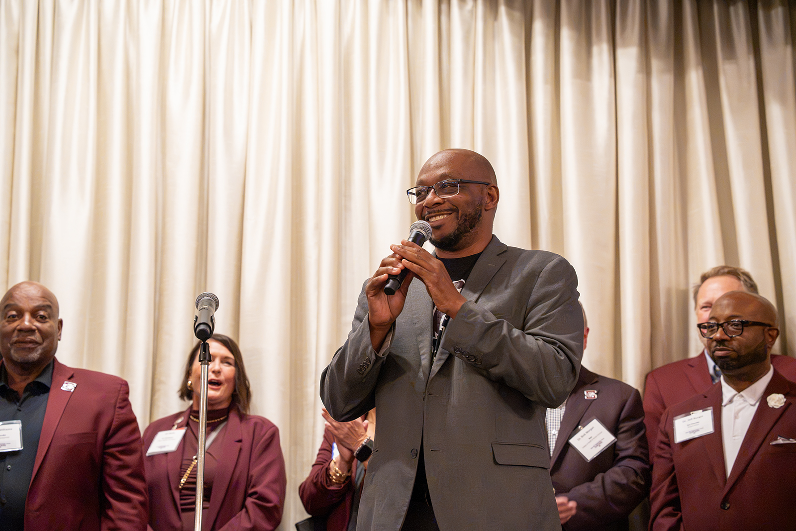Illinois state Rep. William "Will" Davis smiles while speaking into a microphone as SIU leaders and supporters stand behind him during the Saluki Takeover Tour Chancellor's Reception in Chicago.